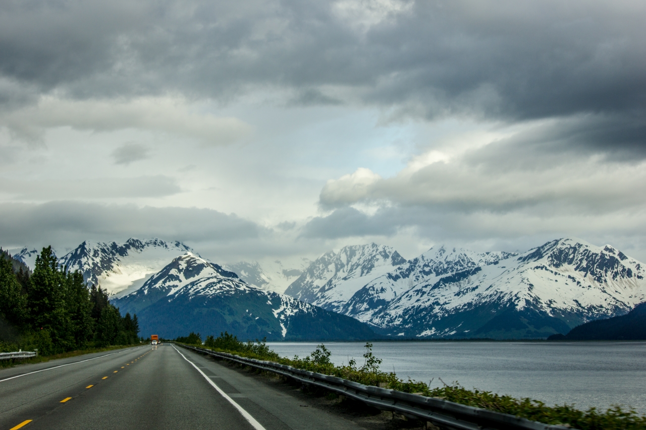 Driving south on Seward Highway (AK 1) in the Chugach National Forest toward the eastern end of Turnagain Arm beyond which lies the snow-covered peaks of Portage Valley where the Kenai and Chugach Mountains meet.