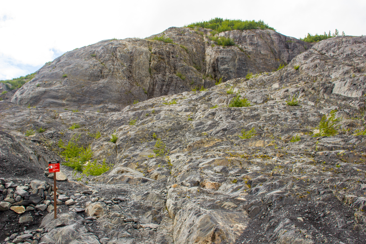 A steep rock face and a sign warning of hazardous conditions at the end of the Edge of the Glacier Trail.