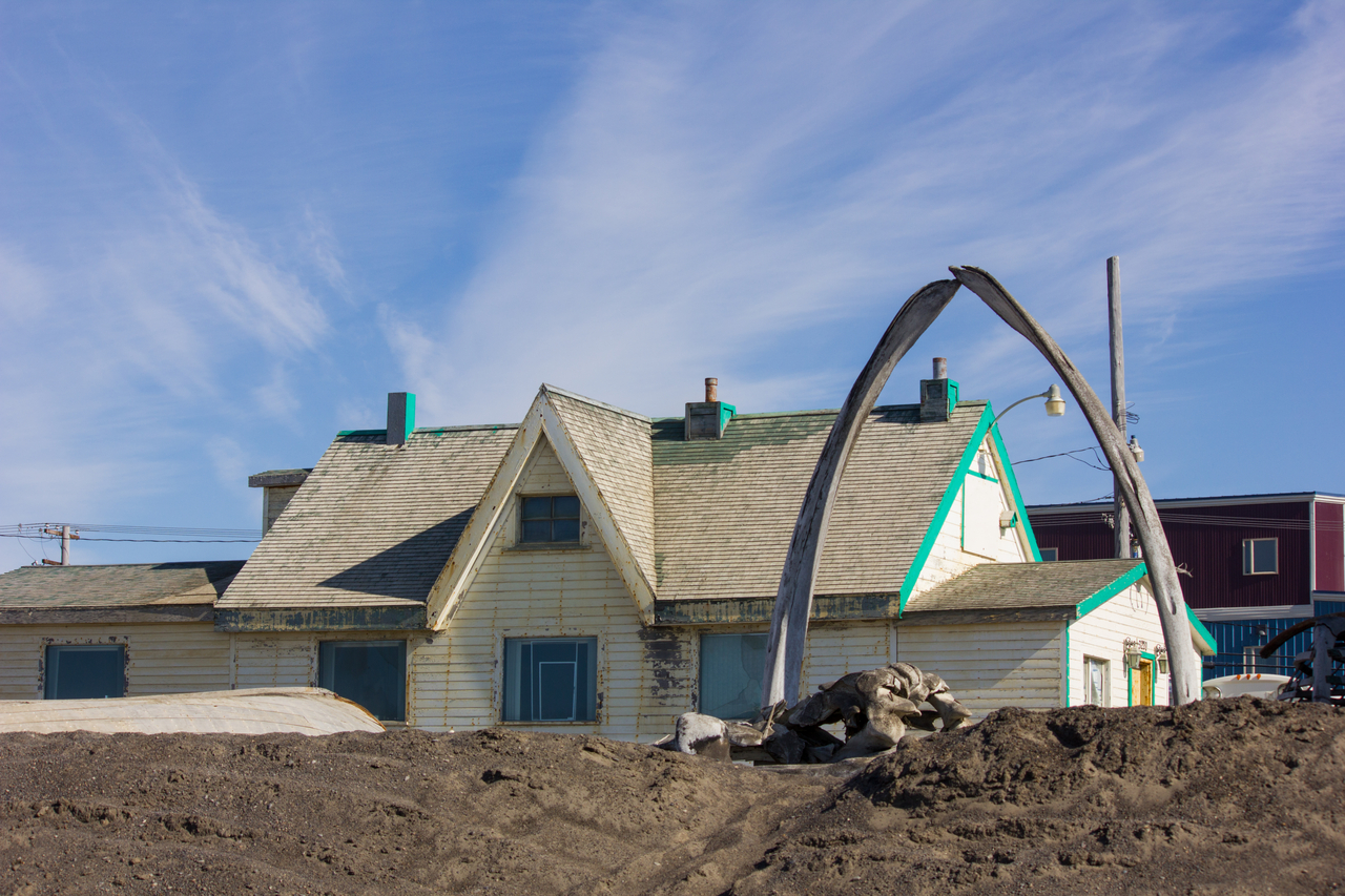The Utqiaġvik bowhead whale (Balaena mysticetus) jaw bone arch along with other whale bones and Point Barrow Refuge Station (1889) from along the shore of the icy Chukchi Sea, Arctic Ocean.