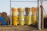 Plastic industrial containers called overpack drums and metal barrels behind a chain link fence at North Slope Borough's Sanitation Services Shop III and thermal oxidation plant.