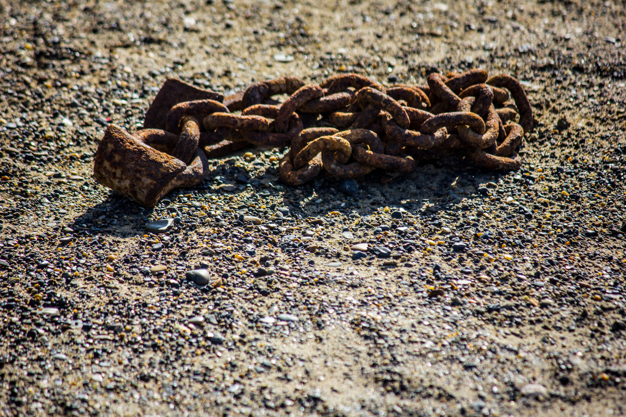 A rusty length of metal link chain on the pebbly ground along the shore of the icy Chukchi Sea, Arctic Ocean.