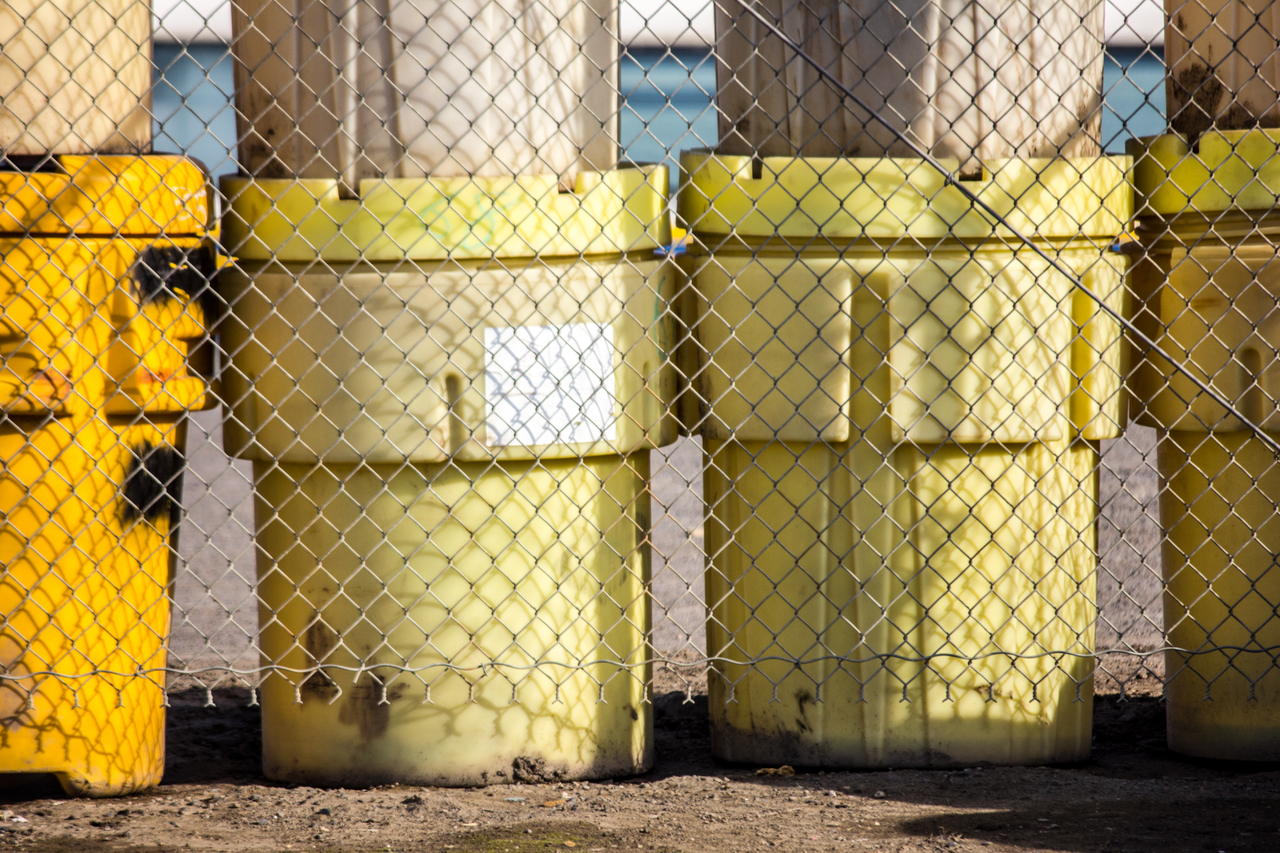 Plastic industrial containers called overpack drums behind a chain link fence at North Slope Borough's Sanitation Services Shop III and thermal oxidation plant.