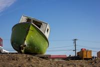 A small, wooden boat painted green and white sitting on a wooden pallet along the shore of the icy Chukchi Sea, Arctic Ocean.