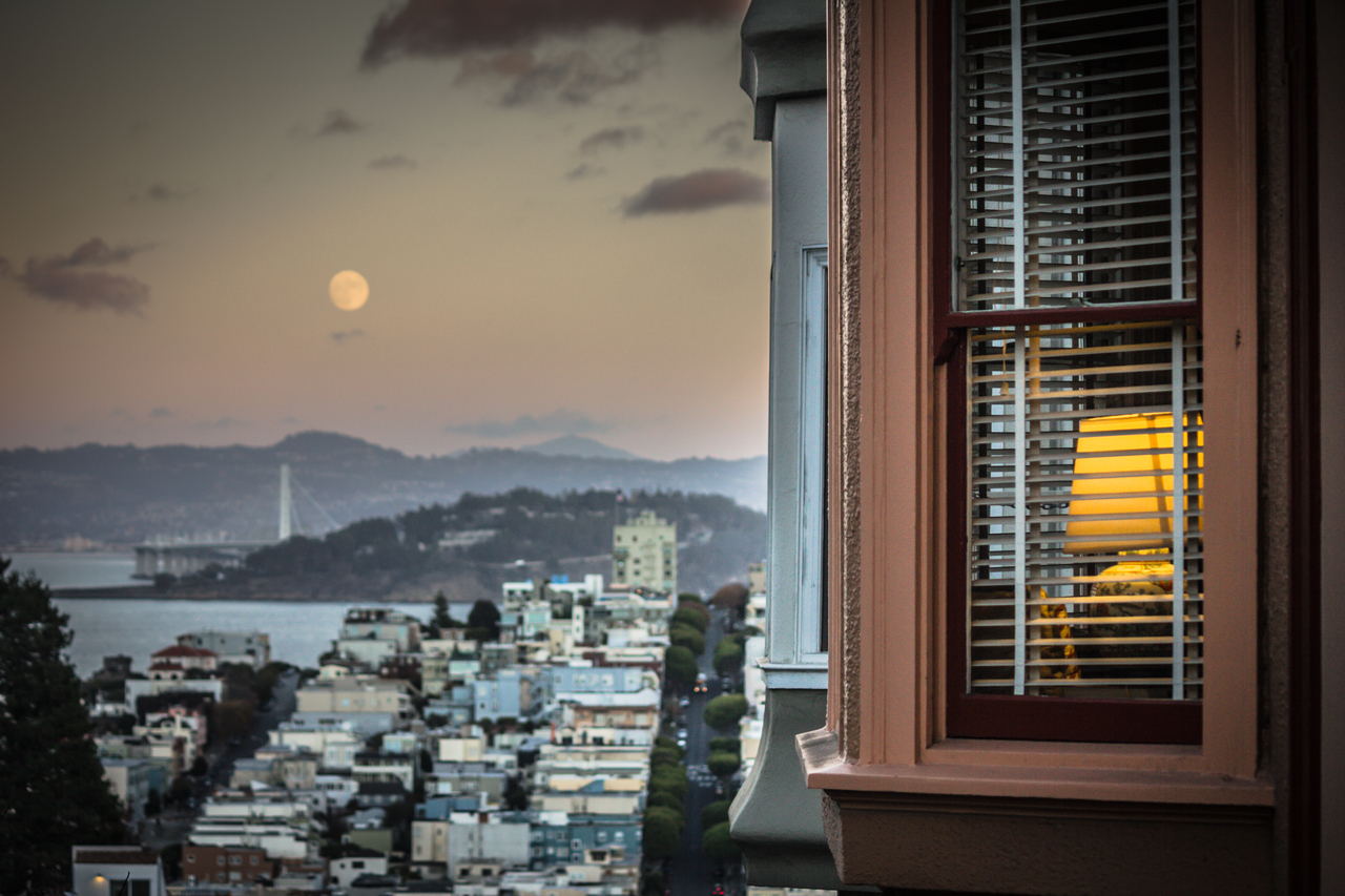 A lamp in a residential bay window, the broccoli block of Lombard Street, Yerba Buena Island, the new eastern span (2013) of the San Francisco–Oakland Bay Bridge (1936) and the nearly full moon beyond.