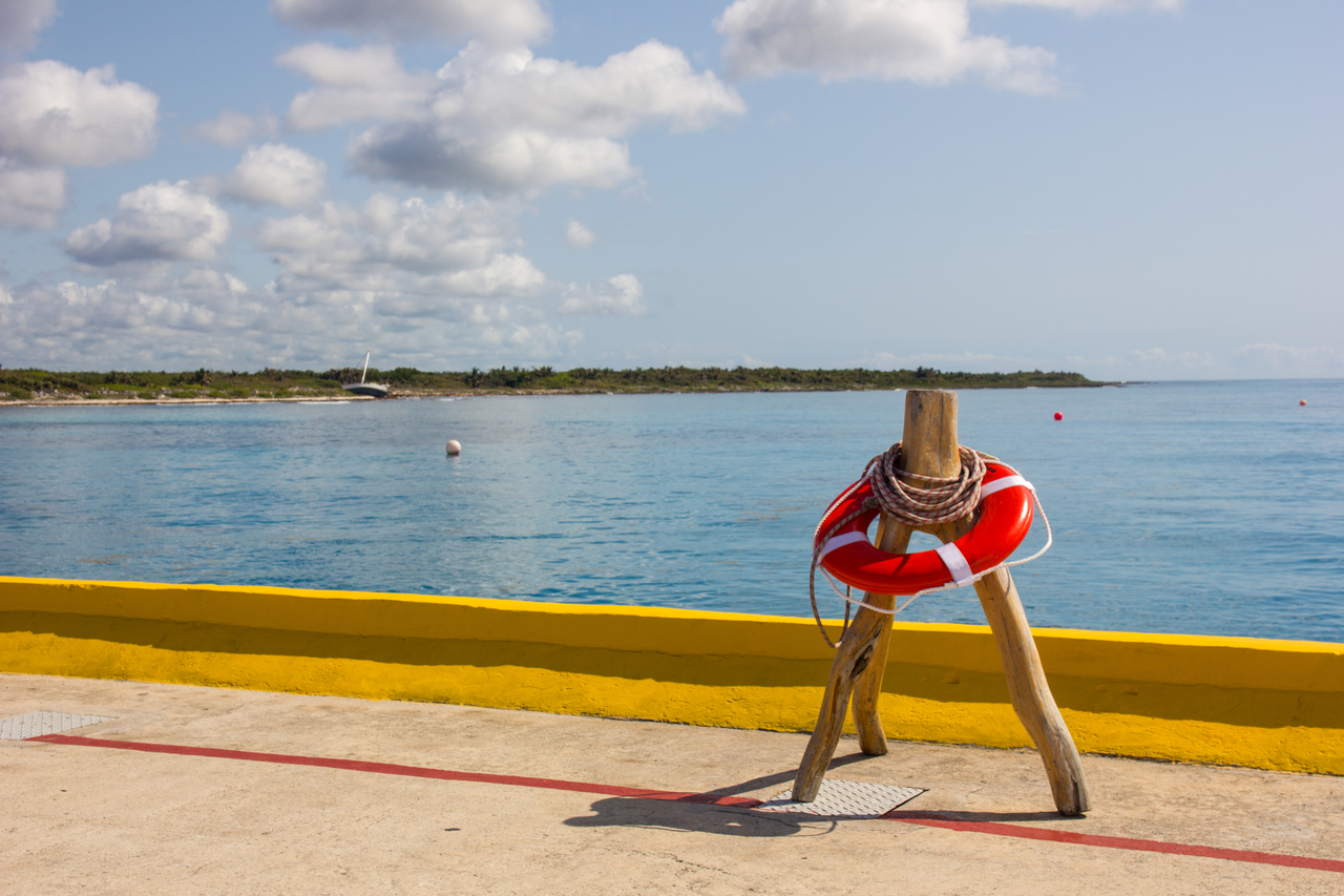 A derelict sailboat washed ashore and a ring buoy on a wooden tripod stand on the cruise ship pier in Costa Maya, Mexico.