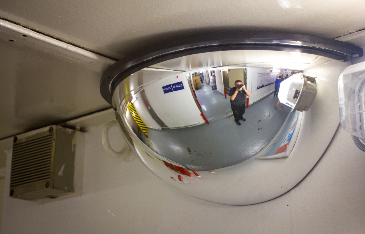 David July reflected in a half-dome convex security mirror at the junction of the main service corridor and Compartments 13 and 14 on Deck 2 during an All Access Tour of the MS Empress of the Seas.