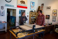 David July operating the press and producing a hand pulled linocut print from a painted linoleum sheet carved with Sutro Tower artwork by Eric Rewitzer.