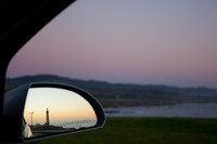 Pigeon Point Lighthouse (1871) and dusk over the Pacific Ocean reflected in the passenger side mirror with grass and the rocky shore beyond.