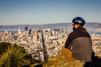 A bicyclist sits atop the northern peak of Twin Peaks looking out over San Francisco on a clear day.