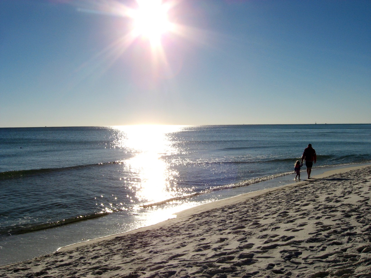 A man walks with a little girl along the Gulf of Mexico surf on the beach behind The Back Porch Seafood & Oyster House.