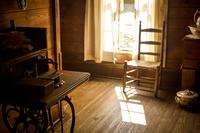 Sunlight beams through a window near a wooden chair and an antique sewing machine in the first floor master bedroom of the Carlton House (1885) at Cracker Country (1978).