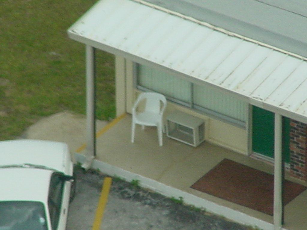 A white resin chair sits alone in front of a motel room next to the Citrus Tower.