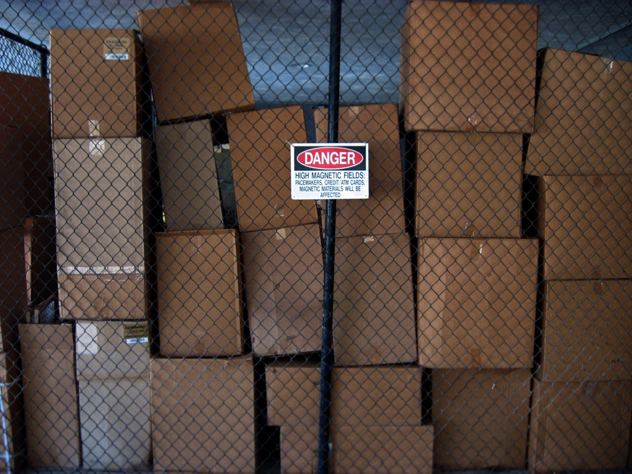 Cardboard boxes, black fence and 'Danger High Magnetic Fields' sign.