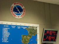 NWS logo, tracking map and a clock in the operations center of the National Hurricane Center.