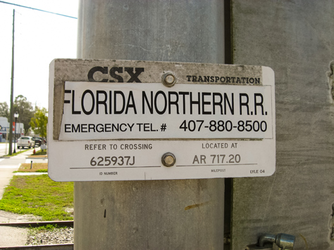 Photo Credit: David July — CSX crossing 625937J identification sign on the northern signal post at the intersection of the old Savannah, Florida and Western Railroad tracks (1884) and Main Street in High Springs, railroad milepost AR 717.20, High Springs, Florida: 19 February 2012