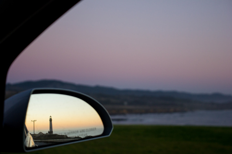 Photo Credit: David July — Pigeon Point Lighthouse (1872) and dusk over the Pacific Ocean reflected in the passenger side mirror with grass and the rocky shore beyond, Pescadero, California, 30 January 2013