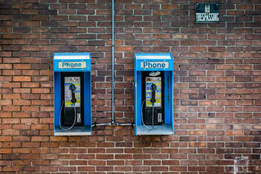 Payphones and a 'no trespassing' sign on the Caroline Street brick wall of Neptune Designs