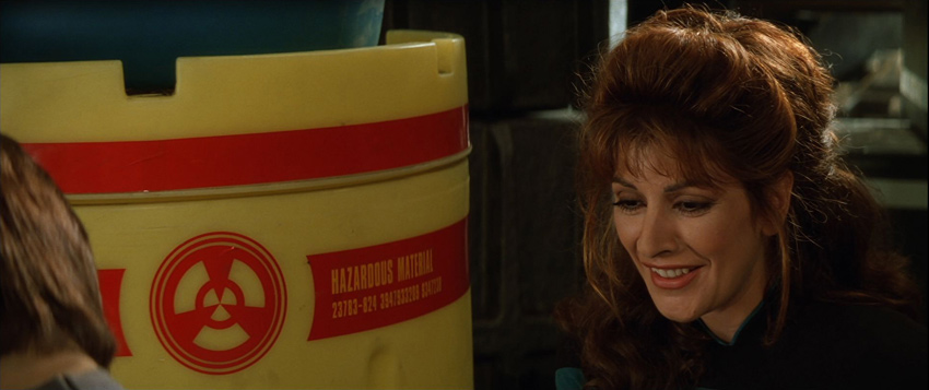 Counselor Deanna Troi next to an overpack drum aboard USS Enterprise
