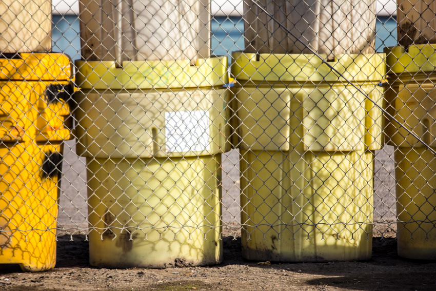 Plastic industrial containers called overpack drums behind a chain link fence at North Slope Borough's Sanitation Services Shop III and thermal oxidation plant