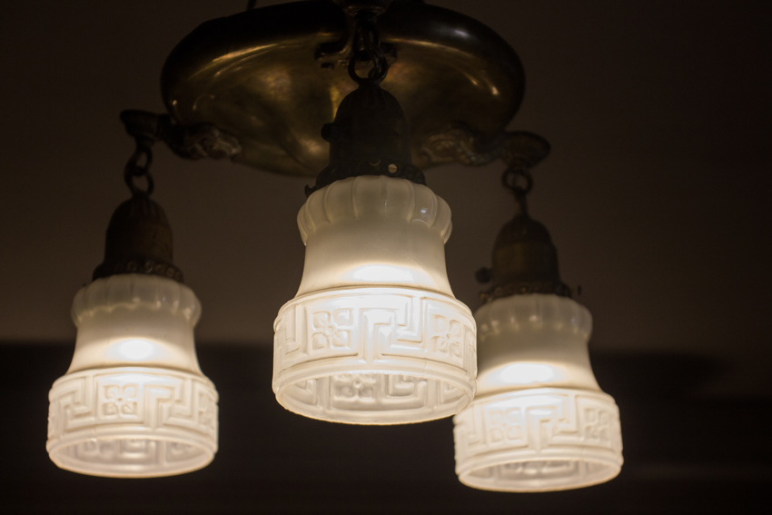 Three light shower-style pan fixture with white pressed glass shades hanging in the front room of the Wickersham House (1904) museum in Pioneer Park.