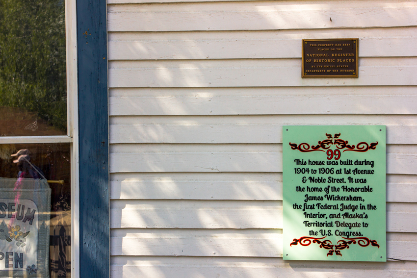 A National Register of Historic Places marker and building description sign mounted to the exterior of the Wickersham House (1904) museum in Pioneer Park.