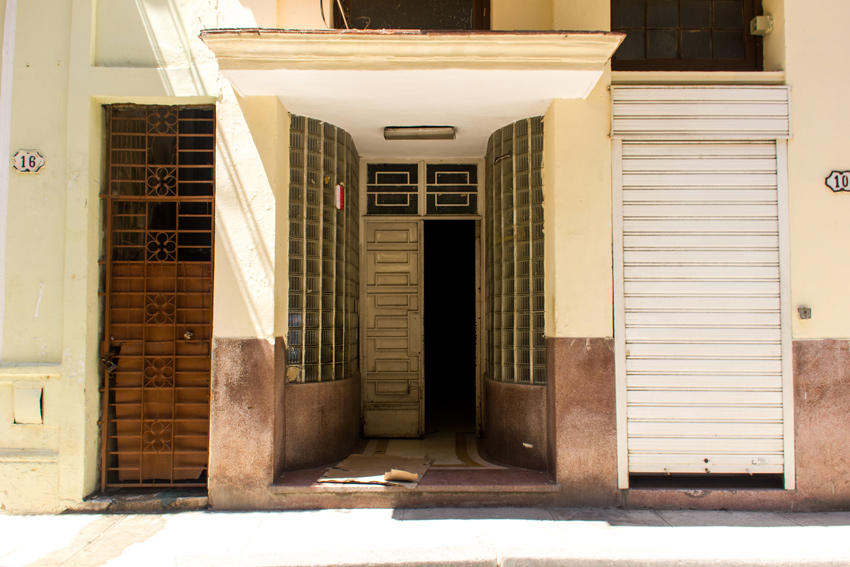 A recessed entranceway walled with glass blocks flanked by a doorway with a tall metal gate and a shuttered doorway in Havana, Cuba