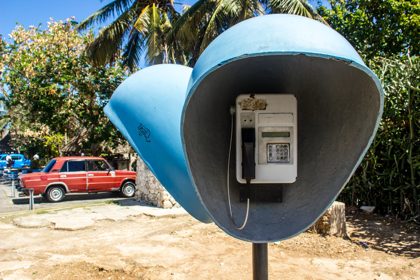 Public telephones across from the Castillo de San Carlos de la Cabaña with a red Lada 1600 beyond in Havana, Cuba