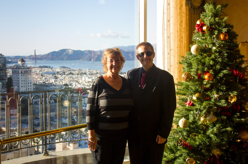 Carol Nichelson and David July pose with the Golden Gate Bridge (1937) beyond and a Christmas tree in the Crown Room lobby on 24F in the Tower Building (1961) of The Fairmont Hotel (1907)